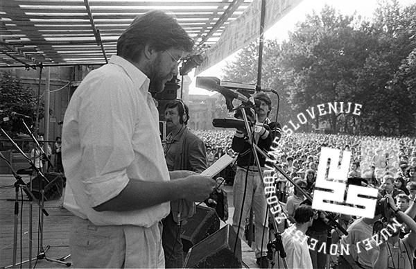 Govornik s papirjem pri mikrofonu pred množico