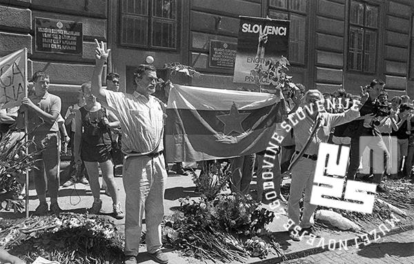 Protest pred stavbo z dvignjeno roko, zastavo in transparenti